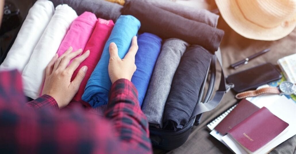 Woman organizing t-shirts on a suitcase before traveling.