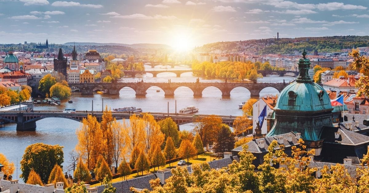 View of the Vltava River, in Prague, crossed by 4 bridges and surrounded by orange and yellow trees.